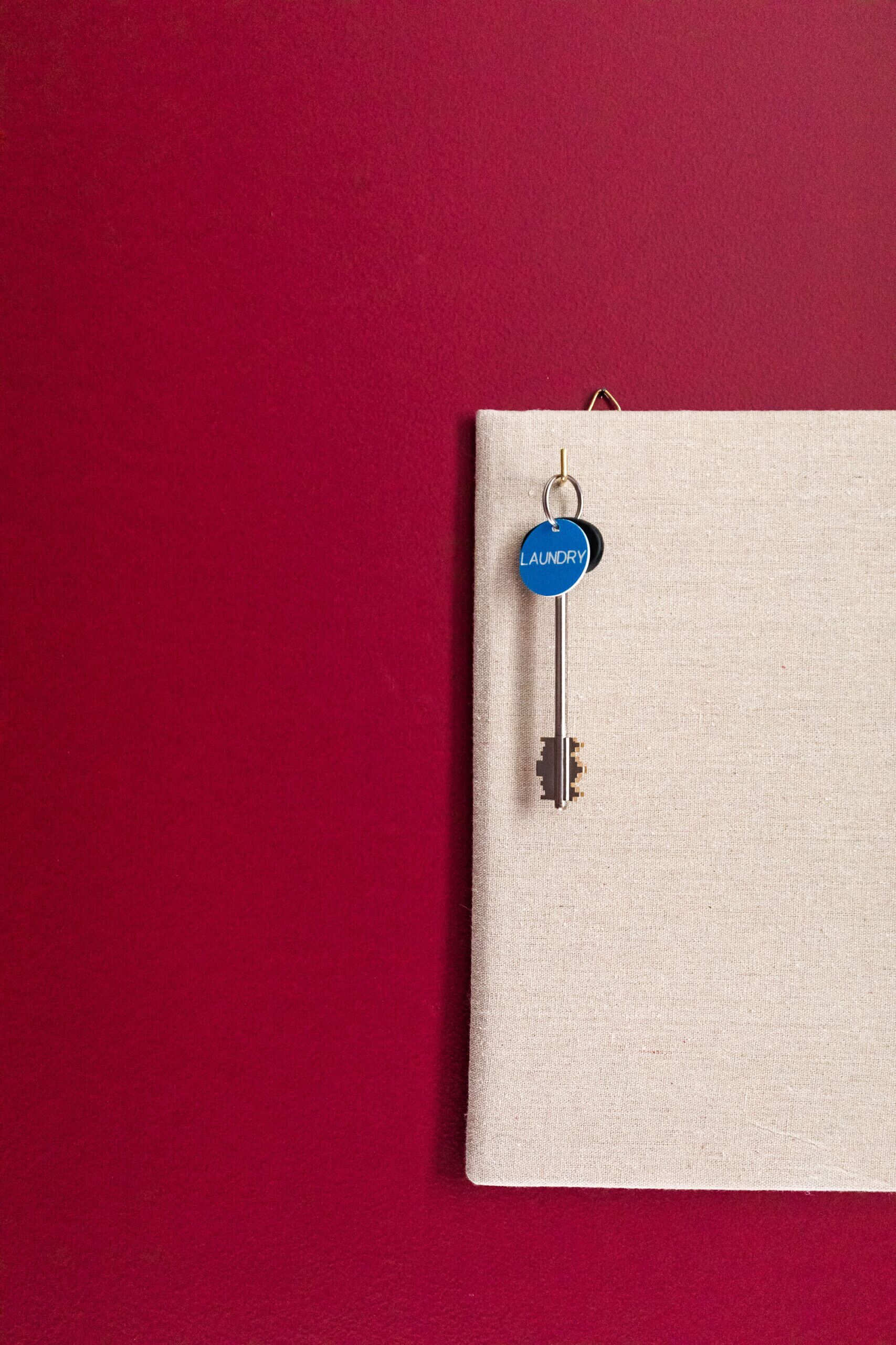 Een sleutel met een blauw labeltje met de tekst 'laundry' hangend op een beige stoffen oppervlak tegen een rode achtergrond.