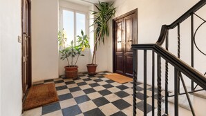 Un pasillo con suelo de cuadros, una puerta de madera, una planta en maceta y una escalera con barandilla de metal.