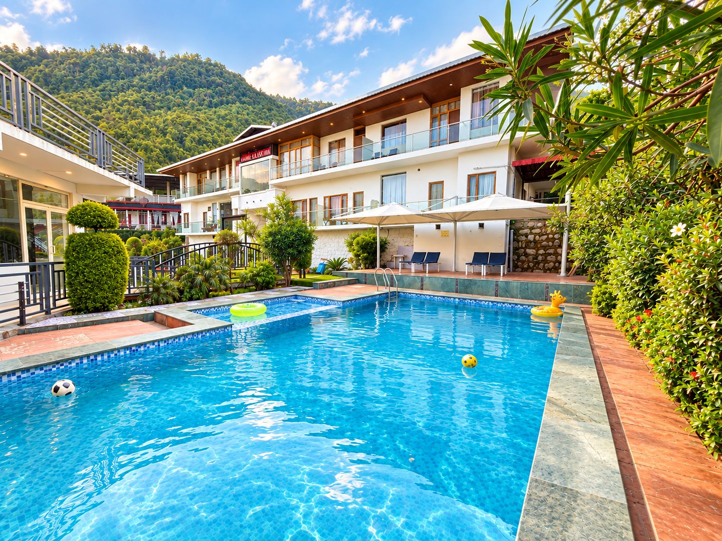 A hotel with a swimming pool, outdoor seating, and a mountain backdrop.