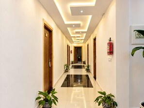 A hotel hallway with a modern design, featuring a glossy floor, wooden doors, and potted plants. - Hotel Luxmi Vilas Inn (Dhanaulti)