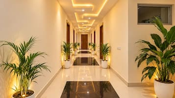 A hallway with a reflective black floor, potted plants, and recessed lighting.