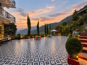 A terrace with a patterned floor, outdoor seating, and a view of the mountains. - Hotel Luxmi Vilas Inn (Dhanaulti)