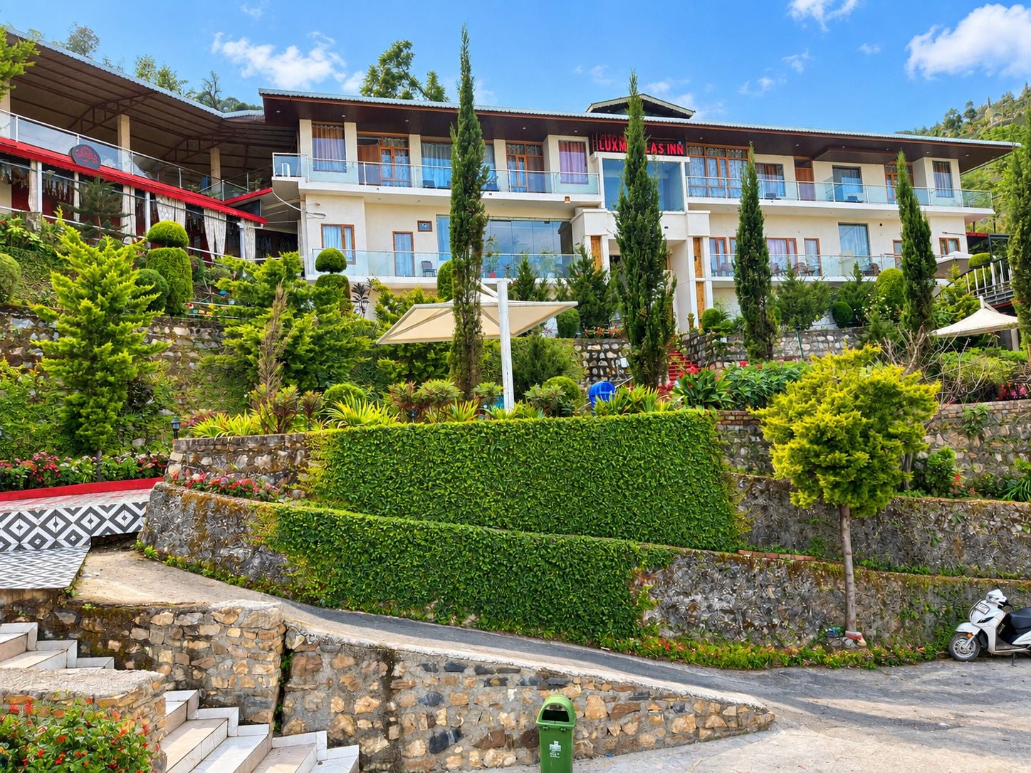 A hotel with multiple balconies, a well-maintained garden, and a stone staircase leading to the entrance.