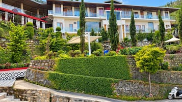 A hotel with multiple balconies, a well-maintained garden, and a stone staircase leading to the entrance.