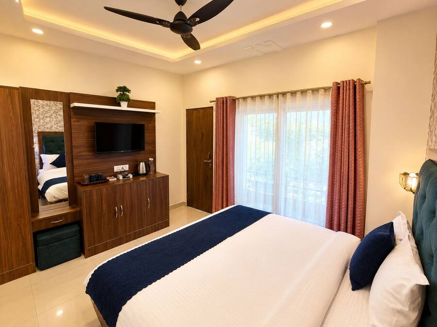 A hotel room with a bed, a television, a wardrobe, a ceiling fan, and a window with curtains.