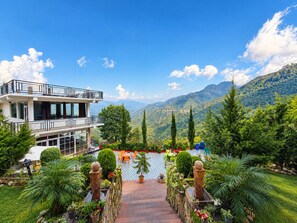 A two-story building with a balcony, surrounded by lush greenery and mountains in the background. - Hotel Luxmi Vilas Inn (Dhanaulti)