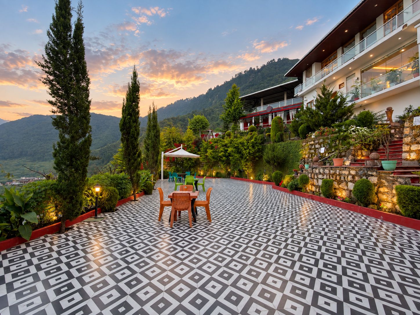 A terrace with patterned flooring, outdoor seating, and a view of a mountainous landscape.