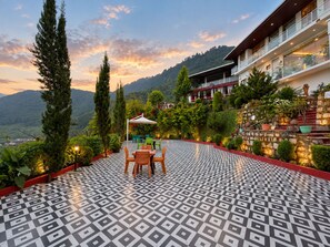 A terrace with patterned flooring, outdoor seating, and a view of a mountainous landscape.