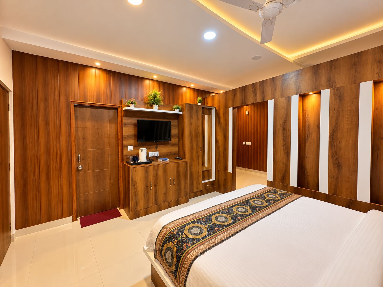 A modern bedroom with a large bed, a TV mounted on a wooden cabinet, and a ceiling fan.