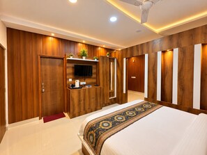A modern bedroom with a large bed, a TV mounted on a wooden cabinet, and a ceiling fan. - Hotel Luxmi Vilas Inn (Dhanaulti)