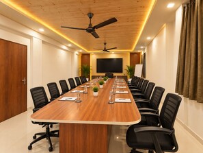 A conference room with a long table, black chairs, a ceiling fan, and a large screen. - Hotel Luxmi Vilas Inn (Dhanaulti)