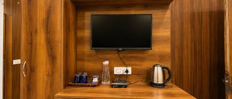 Un mueble de madera con un televisor de pantalla plana montado encima, una tetera y una pequeña planta en un estante.