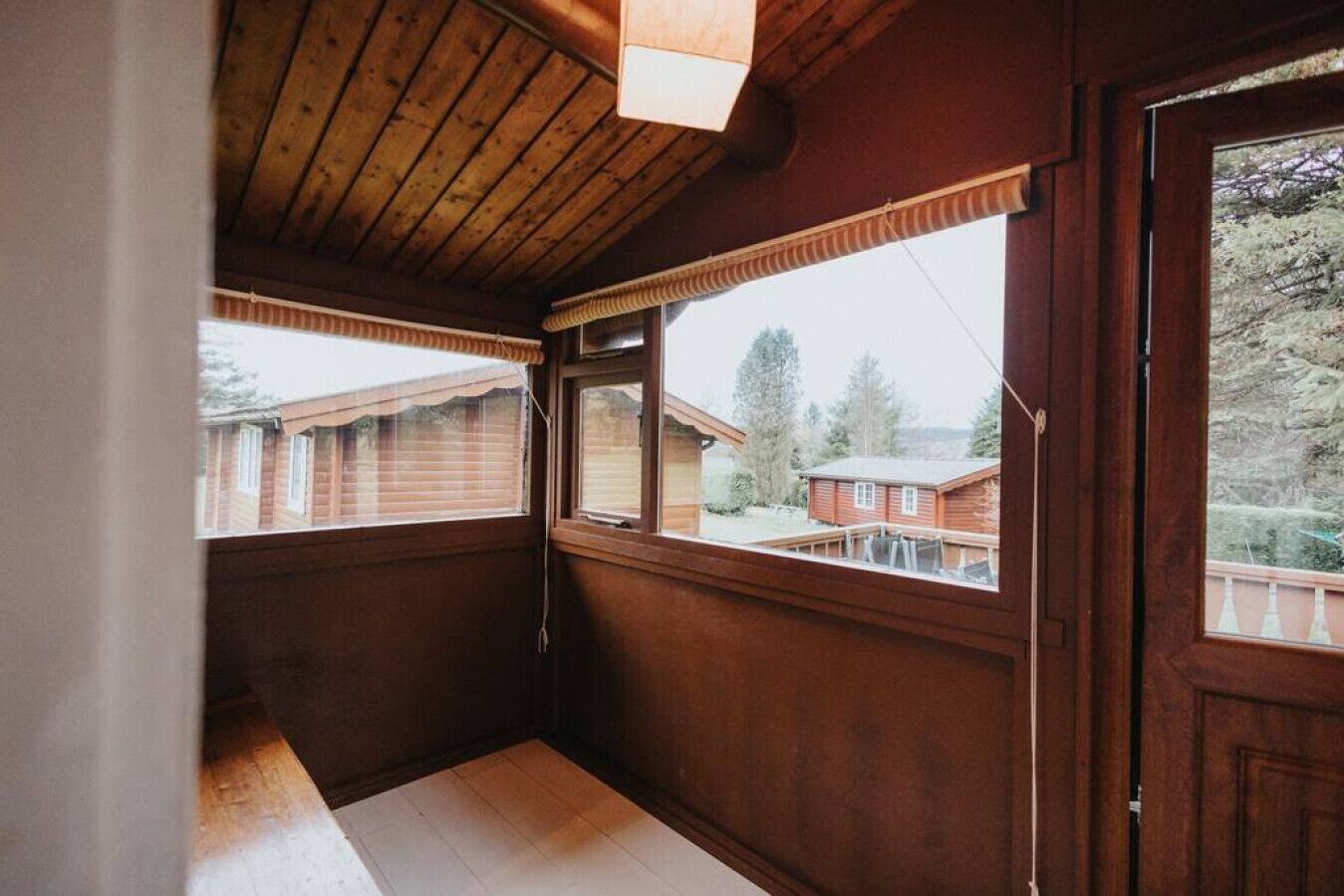 A wooden interior with a sloped ceiling, large windows, and a view of neighboring houses.