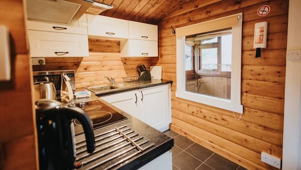 A compact kitchen with wooden walls, white cabinets, a window, and a stove. - Cozy Hideway in Rural Mid Wales (Blaenau Ffestiniog)
