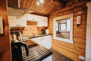 A compact kitchen with wooden walls, white cabinets, a window, and a stove.