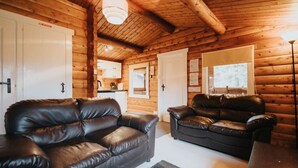 A log cabin interior with two leather sofas, a dining table, and a kitchen area. - Cozy Hideway in Rural Mid Wales (Blaenau Ffestiniog)