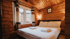A wooden cabin room with a bed, a window with curtains, and a 'Fire Exit Keep Clear' sign. - Cozy Hideway in Rural Mid Wales (Blaenau Ffestiniog)