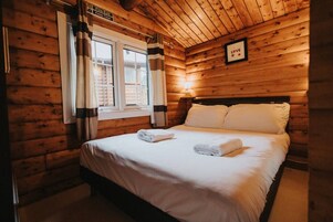 A wooden cabin room with a bed, a window with curtains, and a 'Fire Exit Keep Clear' sign.
