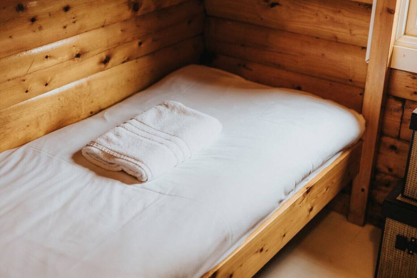 A single bed with a white mattress and a folded white towel.