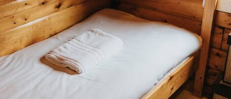 A single bed with a white mattress and a folded white towel.