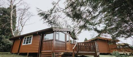A wooden cabin with a balcony and a staircase leading to a deck.