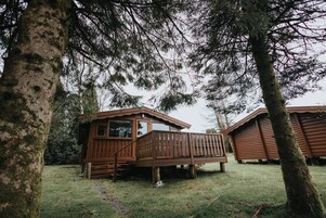 A wooden cabin with a deck, surrounded by trees.