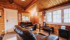A log cabin interior with a leather sofa, a small table, and a window with curtains. - Cozy Hideway in Rural Mid Wales (Blaenau Ffestiniog)