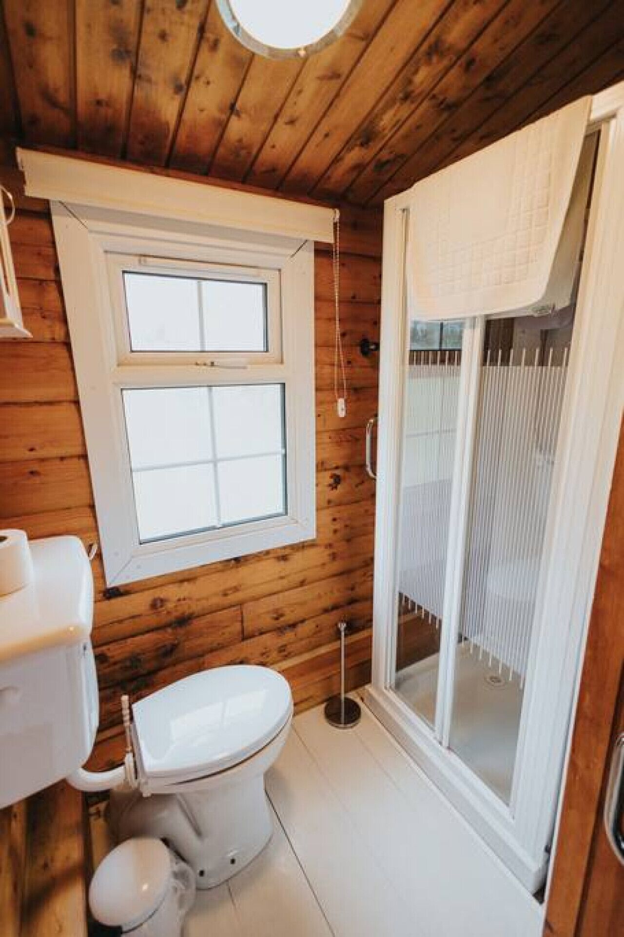 A small, wooden cabin bathroom with a toilet, sink, and a window.