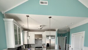 A modern kitchen with white cabinets, a marble countertop, and a central island with stools.