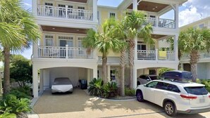A multi-story residential building with a covered garage, two-story balconies, and a driveway with parked cars.