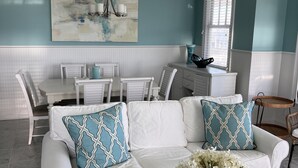 A modern living room with a white sofa, a dining table, and a large abstract painting on the wall.