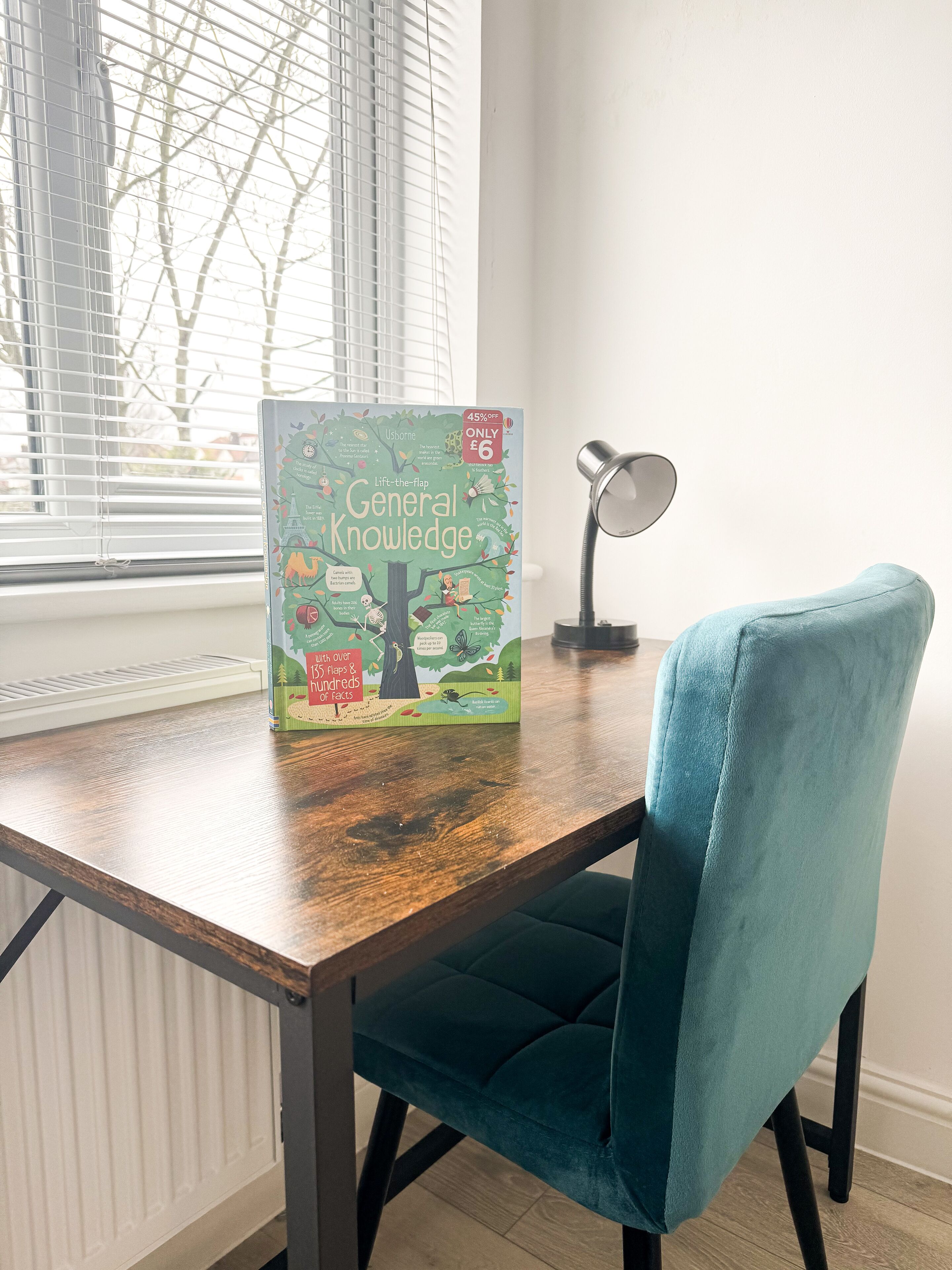 A wooden table with a book titled 'General Knowledge' and a teal chair.
