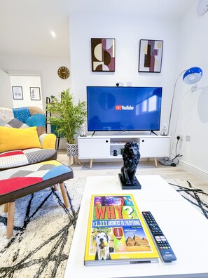 Ein modernes Wohnzimmer mit Flachbildfernseher, einer Couch mit farbenfrohen Kissen, einem Couchtisch mit einer Zeitschrift und einer dekorativen Löwenstatue.