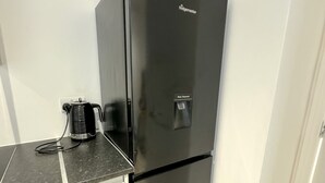 A compact kitchen with a black refrigerator, a coffee maker, and a water dispenser on the countertop. - Perfect 2 bed Apartment 4 Contractors Sleep Upto 5 (London)