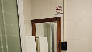 Un baño con lavamanos, espejo, toallero, inodoro y un cartel de prohibido fumar.