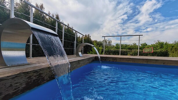 A swimming pool with a waterfall feature, surrounded by a wooden deck and metal railings. - Originale, Elegante e Confortevole Location nei Pressi Della Città Antica (Pompei)