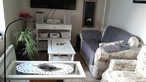 A living room with a flat-screen TV, a clock, a lamp, a sofa, and a coffee table. - Maison Bord de mer (Sarzeau)
