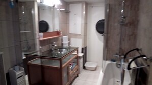 A bathroom with a glass-enclosed sink, a mirror, a shower area, and a toilet. - Maison Bord de mer (Sarzeau)