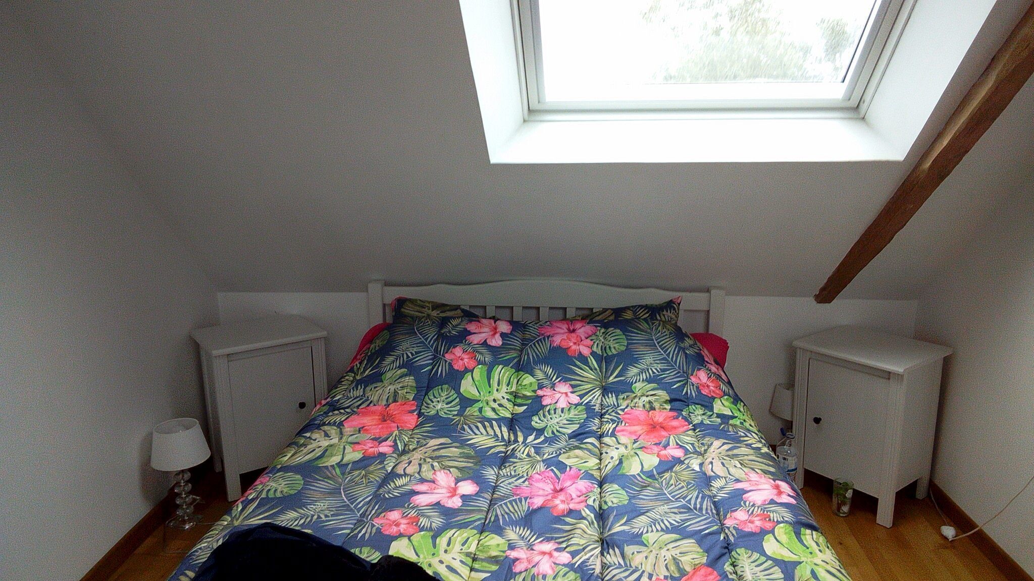 Ein Schlafzimmer mit Oberlicht, einem Bett mit Blumenmuster, zwei Nachttischen und einem Beistelltisch.
