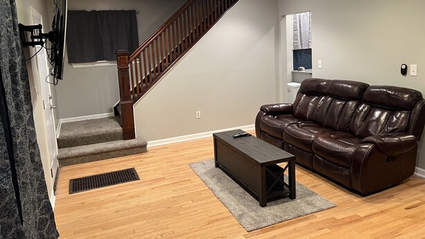 Una sala de estar con un sofá de cuero marrón, una mesa de centro de madera oscura y una escalera con barandillas de madera.