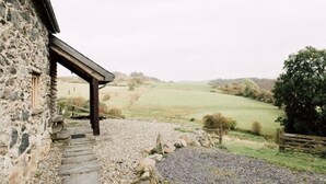 A stone building with a wooden porch overlooking a rural landscape. - Ty Beic Country Apartments, The Barn (Sarnau Bala)