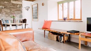 A cozy living room with a stone wall, a wooden bench, a leather couch, and a TV on a wooden stand. - Ty Beic Country Apartments, The Barn (Sarnau Bala)