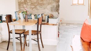A dining area with a wooden table and chairs, a stone wall, and a bookshelf filled with books. - Ty Beic Country Apartments, The Barn (Sarnau Bala)