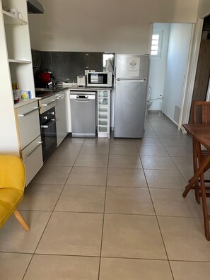 A compact kitchen with a refrigerator, microwave, oven, and a small dining area with a yellow chair.
