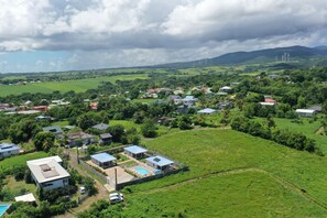 An aerial view of a residential area with houses, a swimming pool, and wind turbines in the background. - Villa Mambia, Terrasse de Vinty. Sainte Rose. (Sainte-Rose)