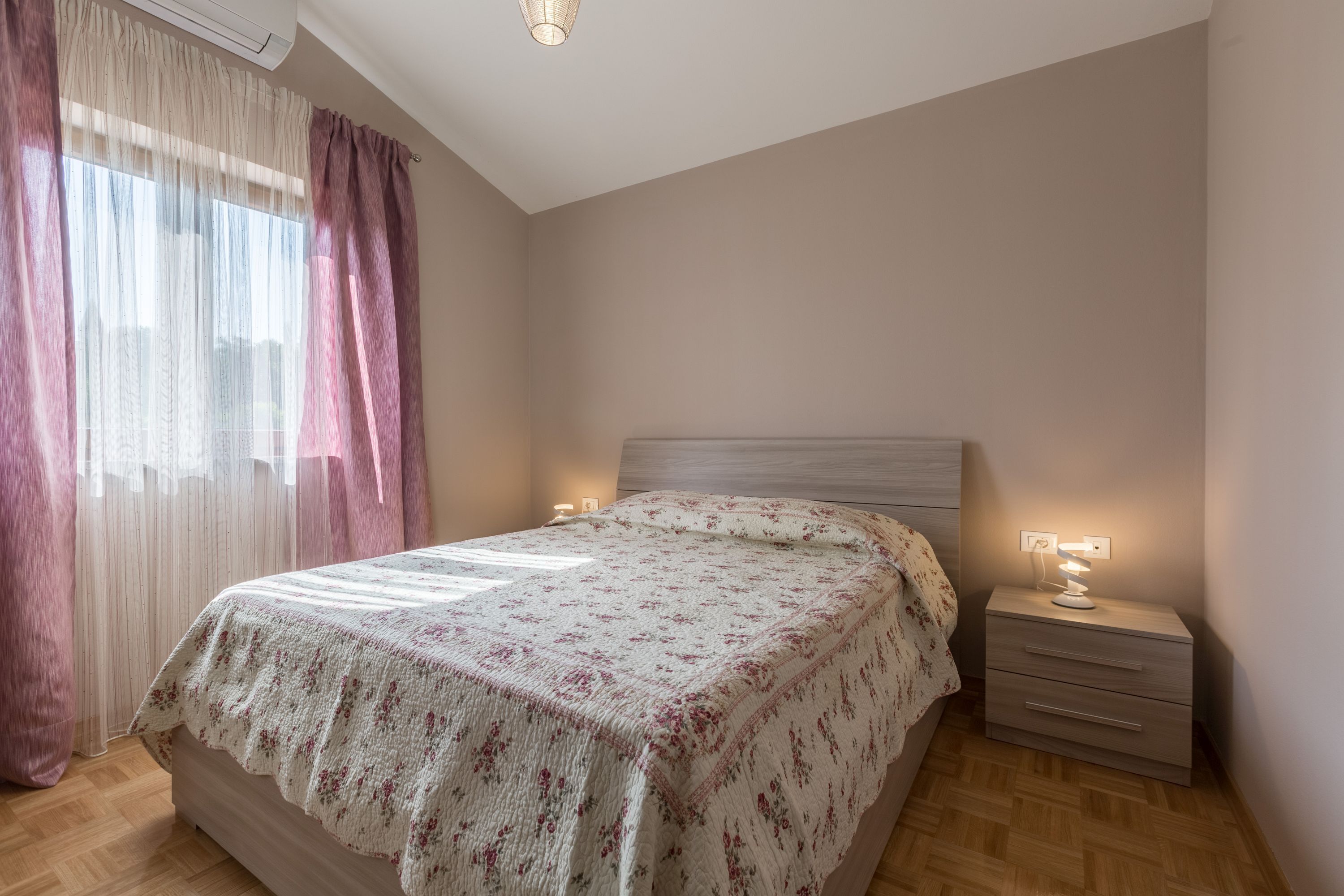 Un dormitorio con cama, una mesita de noche con lámpara y cortinas de encaje.