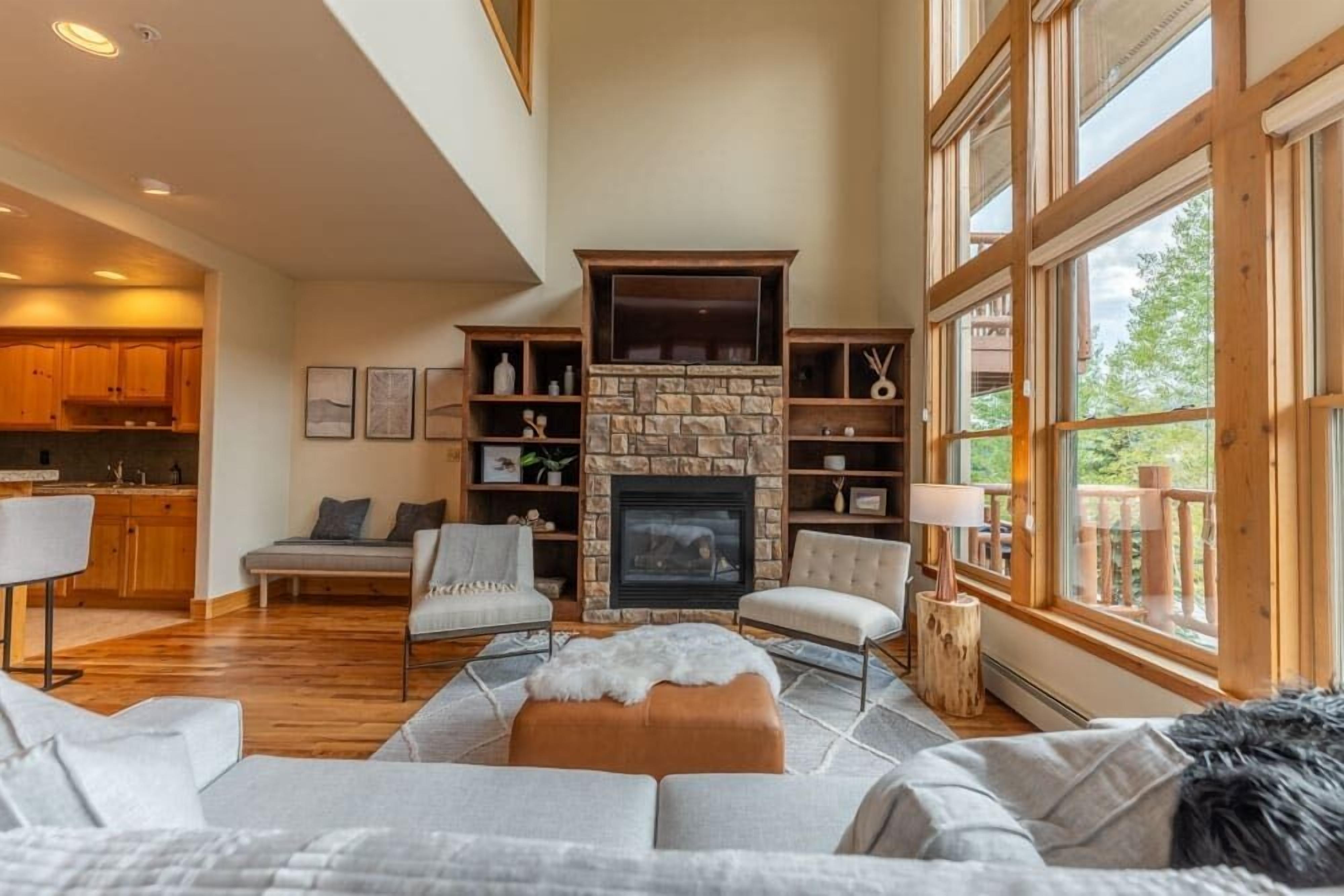 A spacious living area with a fireplace, wooden furniture, and large windows.