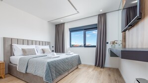 Een moderne slaapkamer met een bed, een televisie, een raam met gordijnen en uitzicht op buiten.