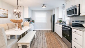 Una cocina moderna con armarios blancos, electrodomésticos de acero inoxidable y una zona de comedor con banco y mesa.