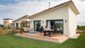 A modern house with a patio area where three people are seated at a table. - Villas Finca La Emperatriz (Baños de Rioja)